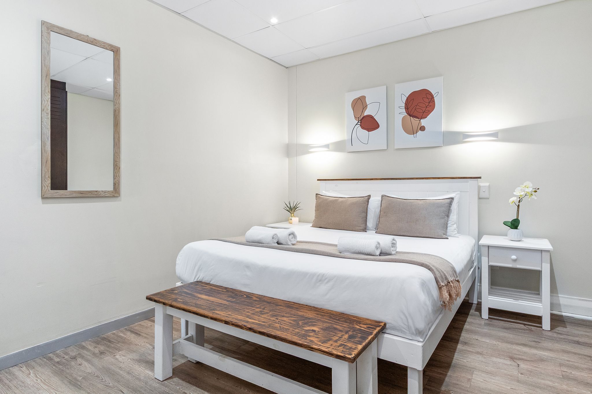 Une chambre à coucher moderne avec un grand lit, des tables de chevet, un banc et des œuvres d’art accrochées au mur.