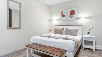 Une chambre à coucher moderne avec un grand lit, des tables de chevet, un banc et des œuvres d’art accrochées au mur.