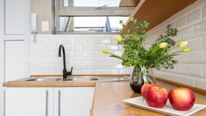 A kitchen with white cabinets, a wooden countertop, a sink, and a vase with flowers and apples. - Greenpark 202 (Cape Town)