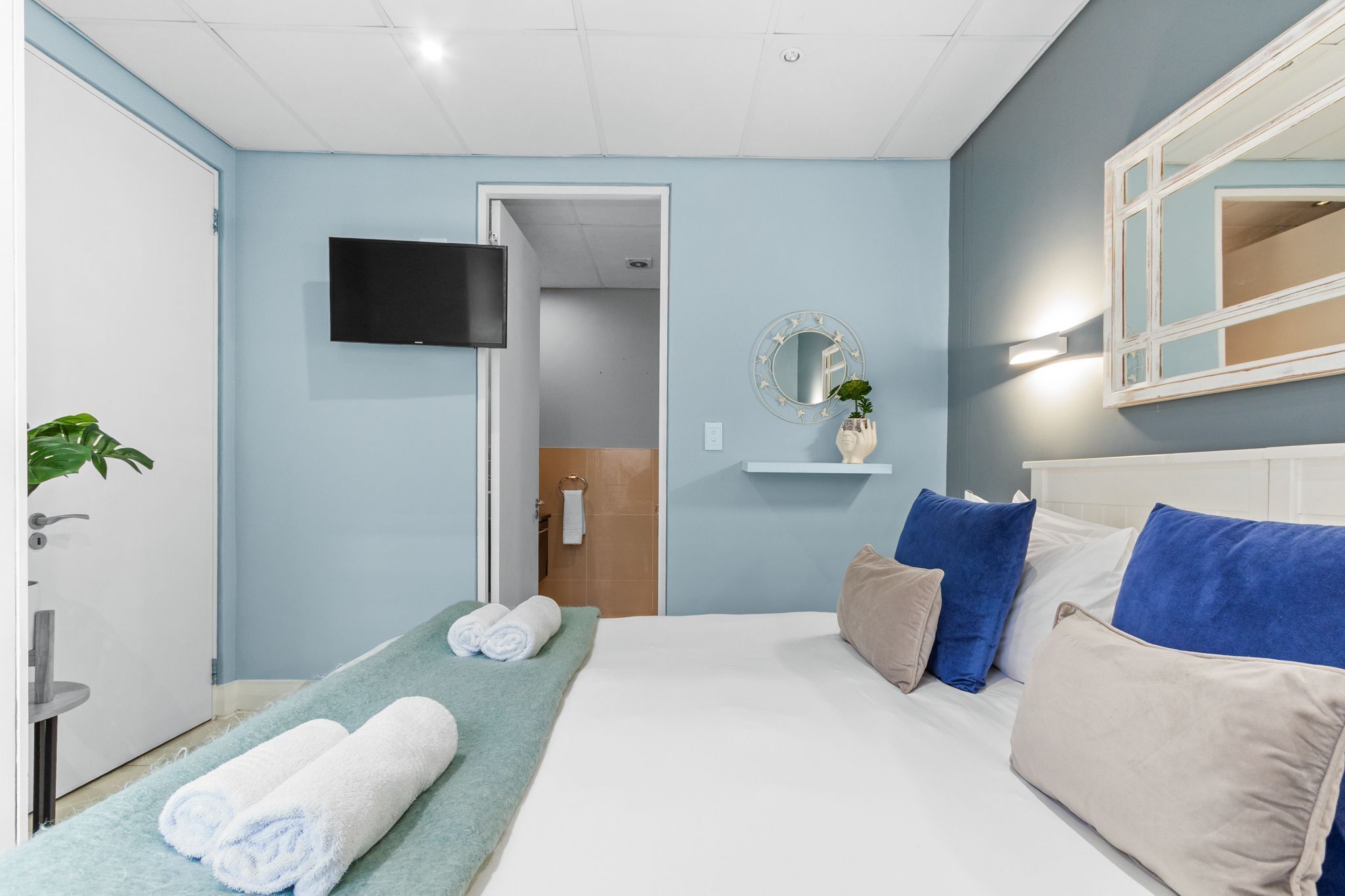 Une chambre d’hôtel avec un lit, une télévision, un miroir et une plante.