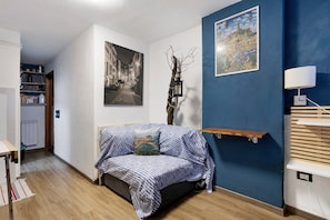 Ein Zimmer mit einem Bett, einer blauen Wand, einem weißen Regal und einem Gemälde.