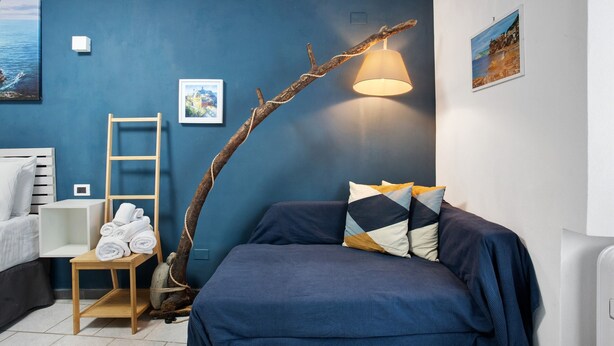 A room with a bed, a chair with towels, a floor lamp, and wall art. - Guest House 'Ca Du Grifun 2' with Wi-Fi and Air Conditioning (Vernazza)