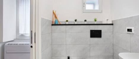 A modern bathroom with a bidet, toilet, and a shelf with plants and toiletries.
