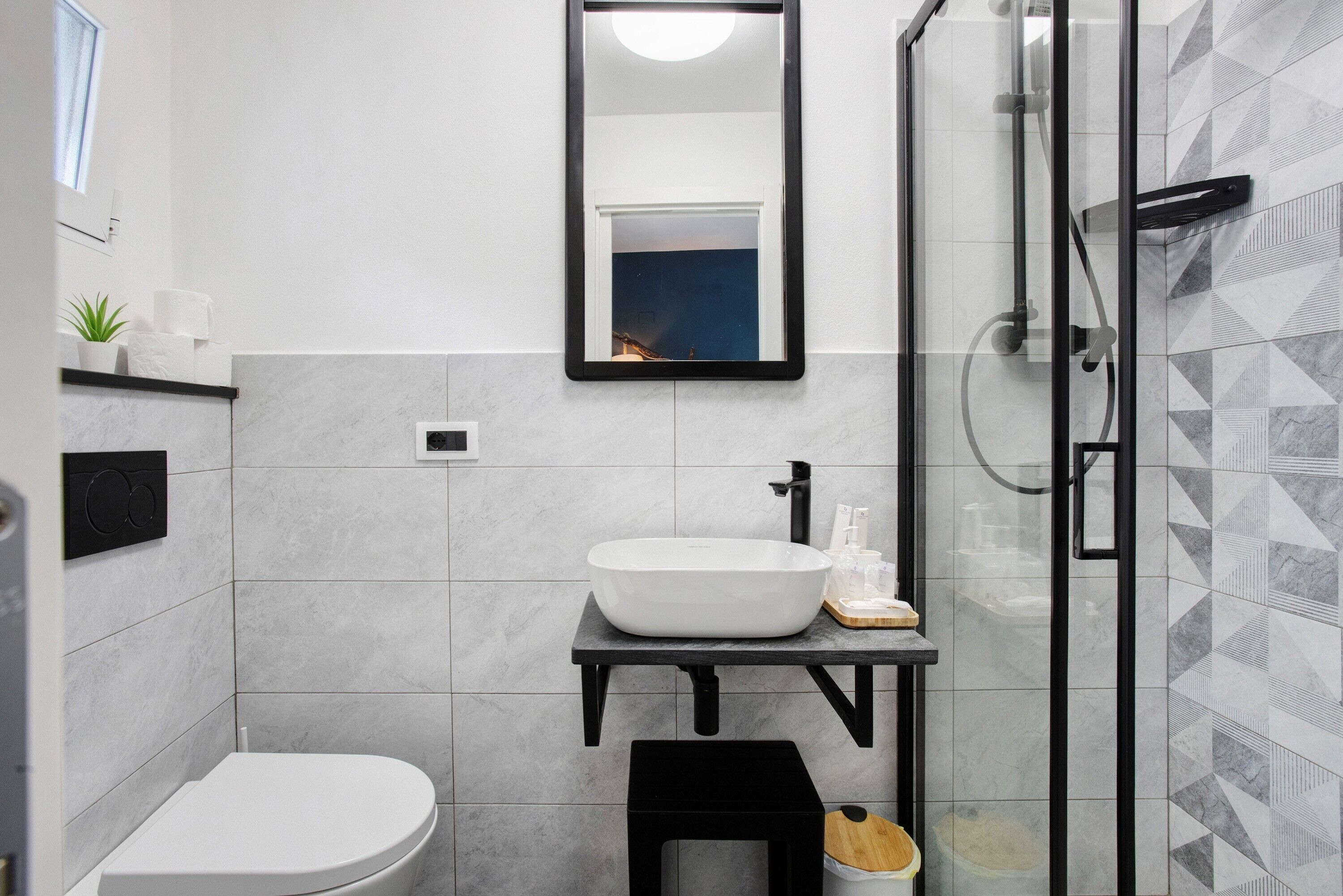 A modern bathroom with a white sink, a black vanity, a glass shower enclosure, and a toilet.