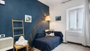 A bedroom with a bed, a chair with towels, a ladder, a wall-mounted lamp, and a window with curtains. - Guest House 'Ca Du Grifun 2' with Wi-Fi and Air Conditioning (Vernazza)