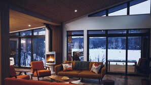 A cozy living room with a fireplace, large windows, and a view of a snowy landscape.