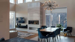 A modern dining area with a fireplace, large windows, and a contemporary chandelier.