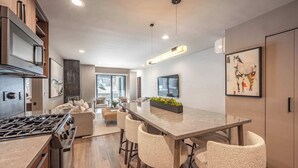 Una cocina moderna con una isla central, taburetes de bar y una zona de comedor con una mesa grande.