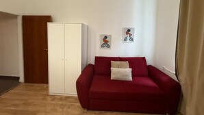 A room with a red sofa, a white wardrobe, and two abstract wall art pieces. - Stylish 1BR Apartment Near Westbahnhof (Vienna)