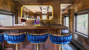 Zona de bar con mostrador de madera, taburetes de terciopelo azul y un espejo grande sobre el mostrador.