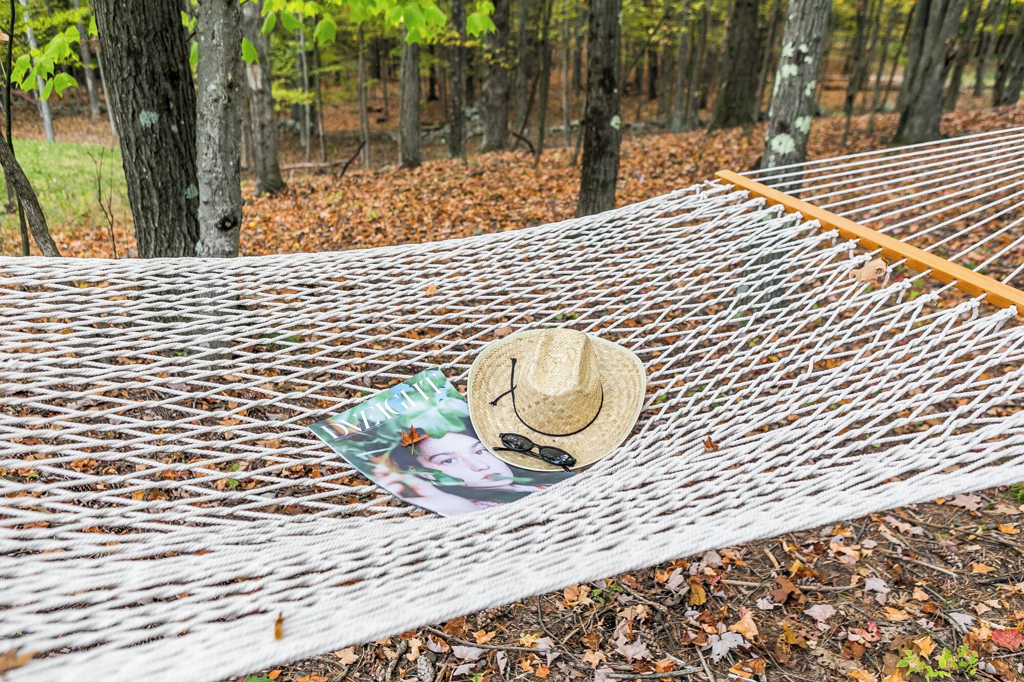 Un hamac dans une forêt, avec un chapeau et des lunettes de soleil posés dessus.