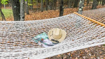 Un hamac dans une forêt, avec un chapeau et des lunettes de soleil posés dessus.