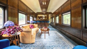 Interior de un vagón de tren con sofá, zona de bar y grandes ventanales.