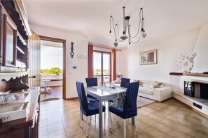 A dining area with a table and chairs, a sofa, a fireplace, and a view through a door.