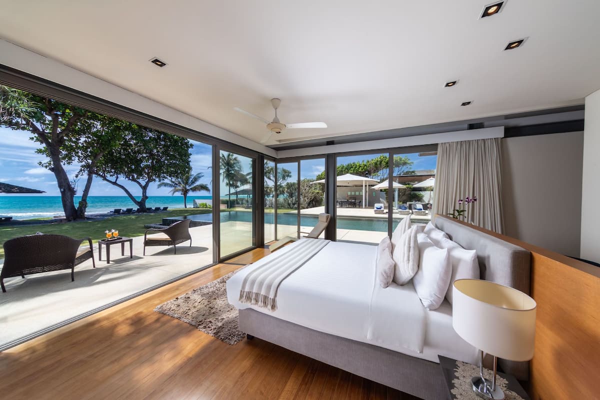 Une chambre moderne avec un grand lit, une vue sur l’océan et un espace patio aménagé avec du mobilier d’extérieur.