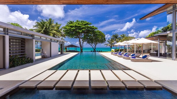 A modern infinity pool with clear blue water, surrounded by lounge chairs and umbrellas, with a view of the ocean and palm trees. - Villa Cielo (Takua Thung)