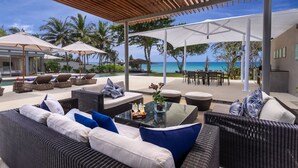 A covered outdoor seating area with wicker furniture, a glass table, and umbrellas providing shade. - Villa Cielo (Takua Thung)