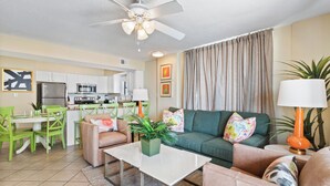 A modern living room with a green sofa, a coffee table, and a dining area with green chairs. - Seaside Beach & Racquet 4912 (Orange Beach)