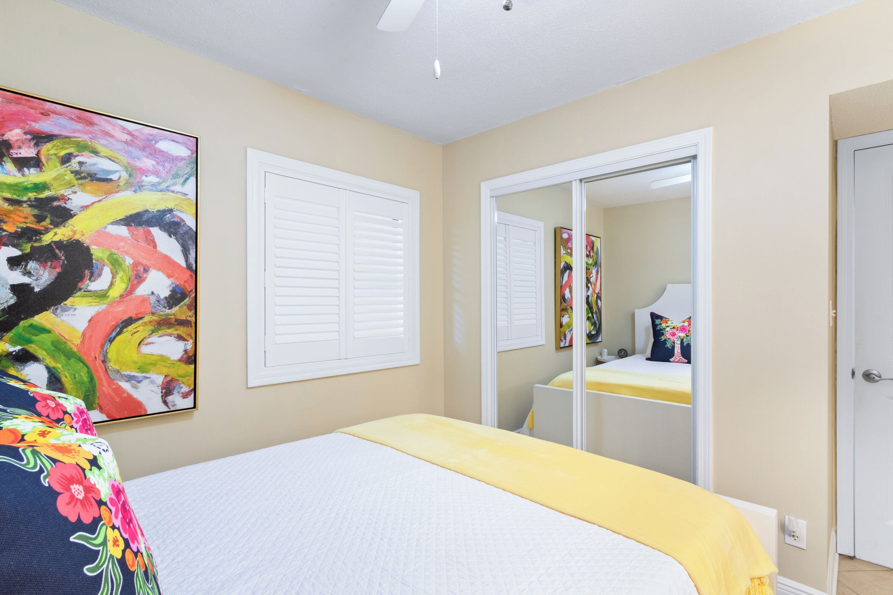 A bedroom with a bed, a large mirror, and a colorful abstract painting on the wall.