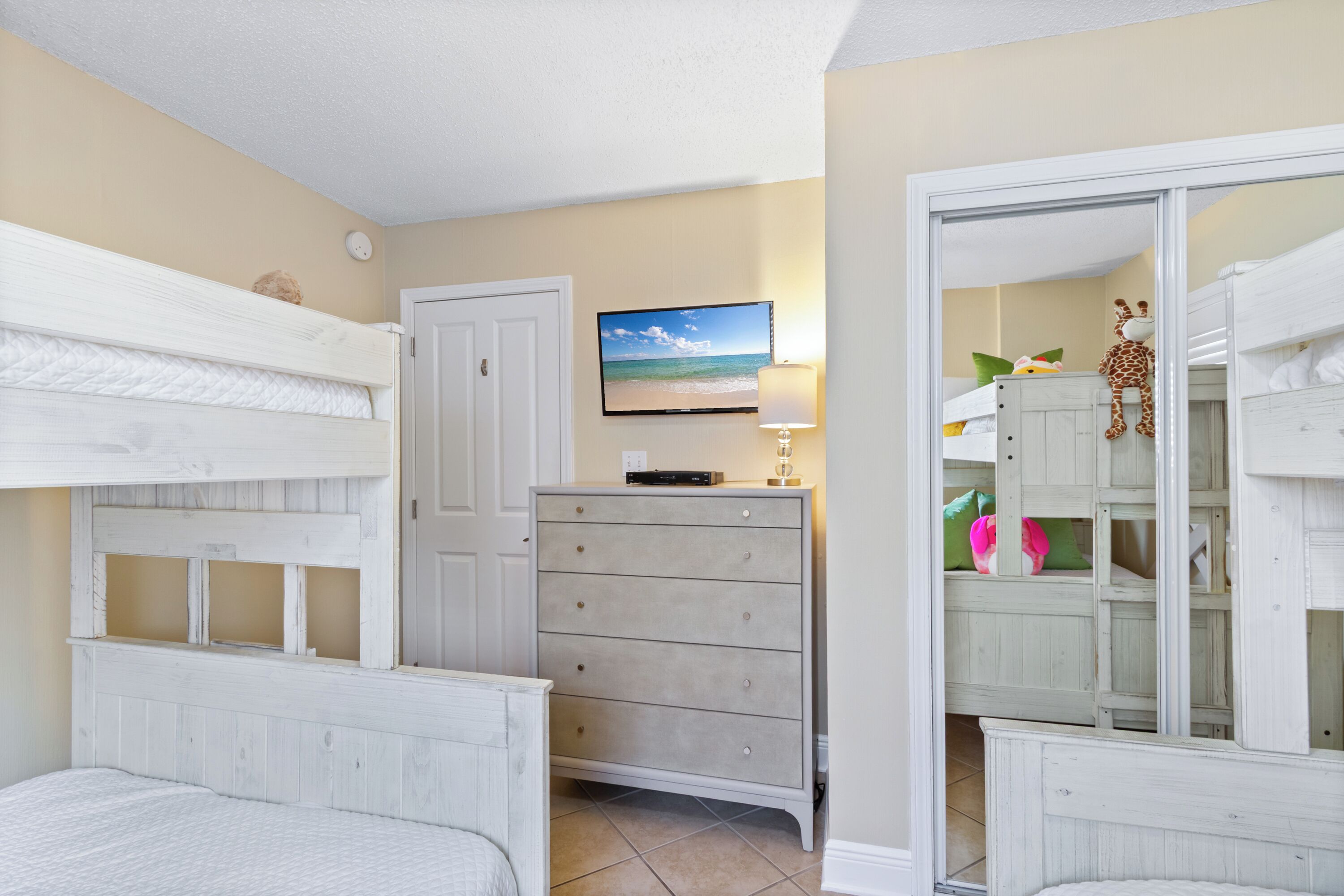 Une chambre avec des lits superposés, une commode, un téléviseur et un miroir.