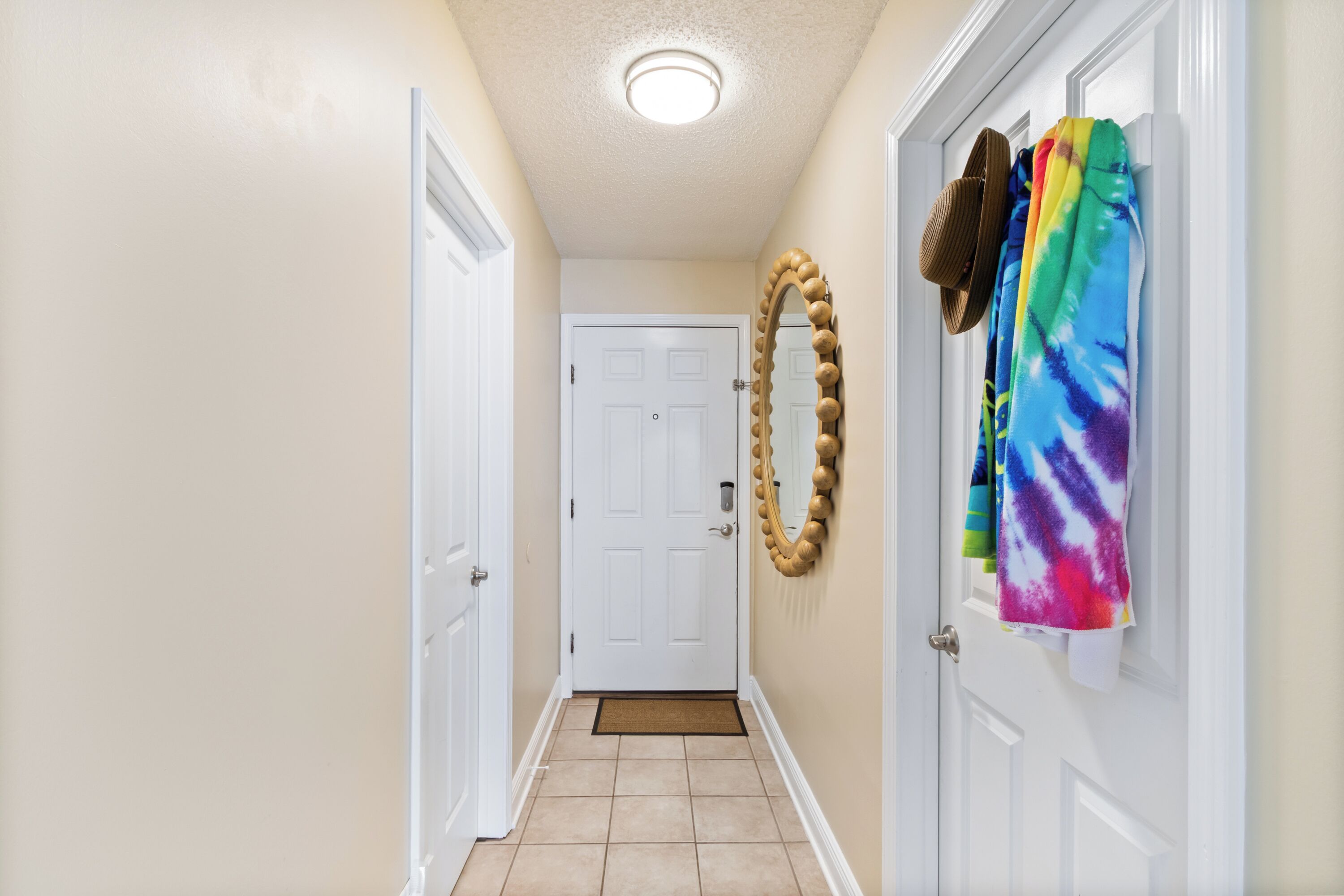 A hallway with a white door at the end, a mirror on the wall, and a colorful towel hanging on the door.