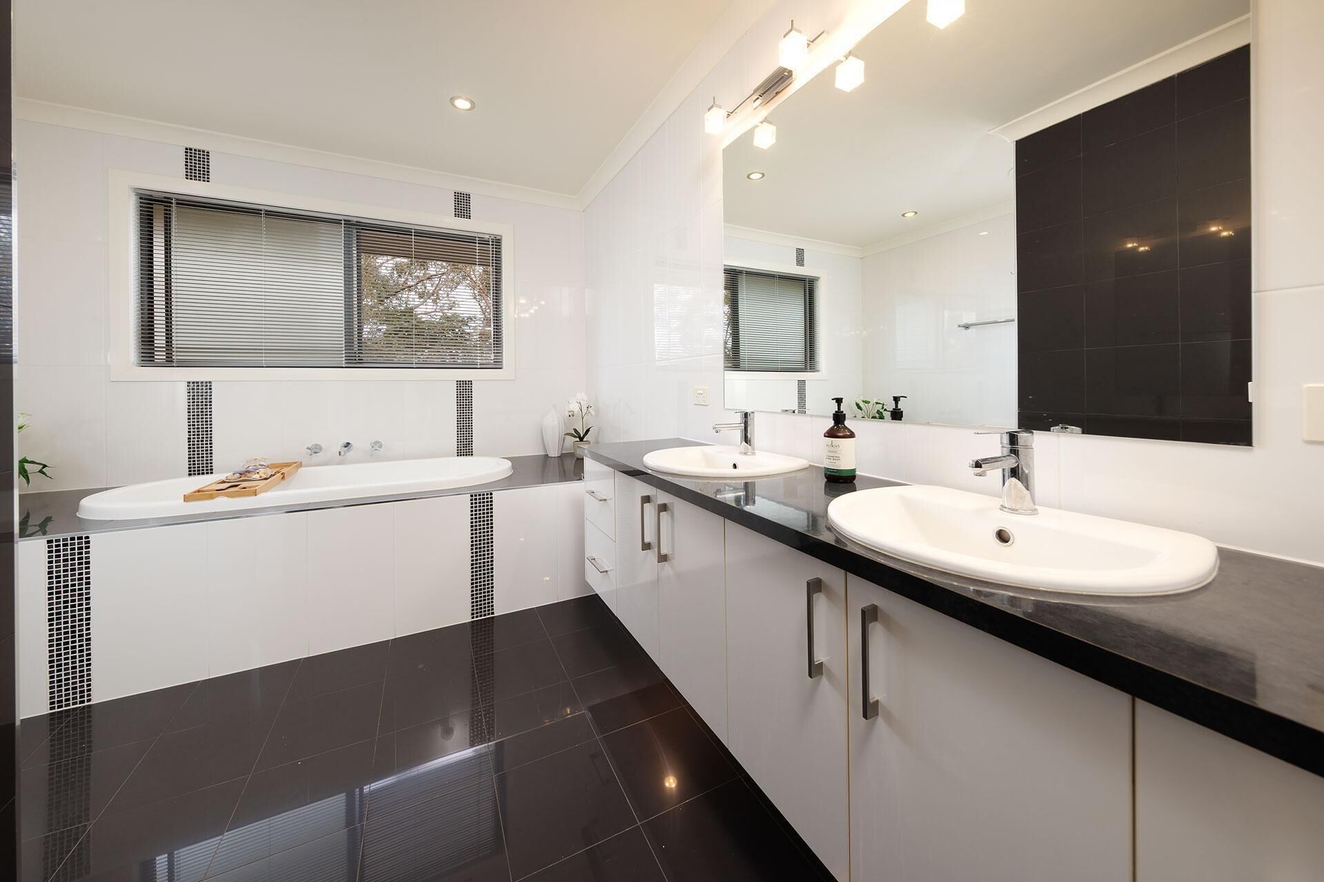 A modern bathroom with two sinks, a large mirror, and a window with blinds.