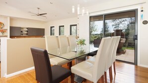A modern dining area with a glass table, white chairs, and a ceiling fan. - Peregrine Pool Paradise - Outstanding four bedroom family home with pool! (Wodonga)