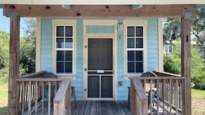 A wooden porch with a door, two windows, and a sign above the door.