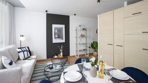 A modern living room with a sofa, coffee table, dining table set for two, and a bookshelf. - La Pergola 5A - Double Studio Exterior (Castellón)