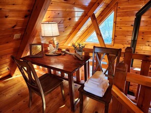 A wooden interior with a table and chairs, a lamp, and a window.