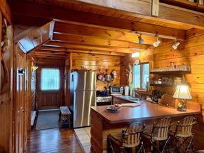 A wooden cabin interior with a kitchen, dining area, and a small entryway.