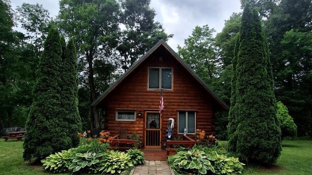 Une cabane en bois avec une entrée centrale, entourée de jardins bien entretenus et de grands arbres.