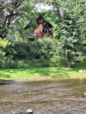 Eine Hütte, umgeben von dichtem Grün und einem Bach.