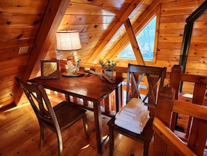 A wooden interior with a table and chairs, a lamp, and a window.