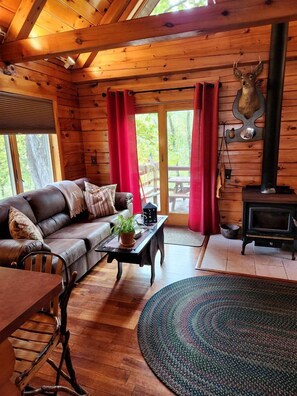 A wooden cabin interior with a sofa, a table, a rug, a fireplace, and a deer head decoration.