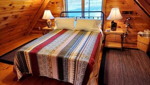Une chambre confortable située sous les toits, avec un grand lit, deux lampes de chevet, une commode en bois et une fenêtre donnant sur les arbres.