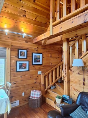 A wooden interior with a staircase, framed pictures, a table, and a leather sofa.