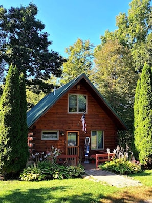 A wooden cabin with a porch, a flag, and a well-maintained garden.