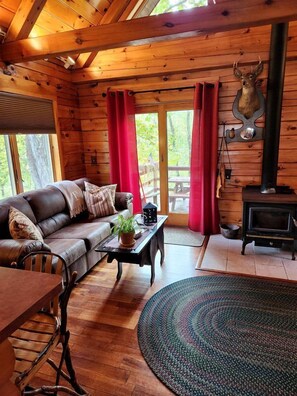 Interior de una cabaña de madera con sofá, mesa, alfombra, chimenea y una decoración de cabeza de venado.
