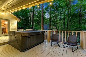 Una terraza de madera con un jacuzzi, dos sillas de mimbre y vistas a un bosque.