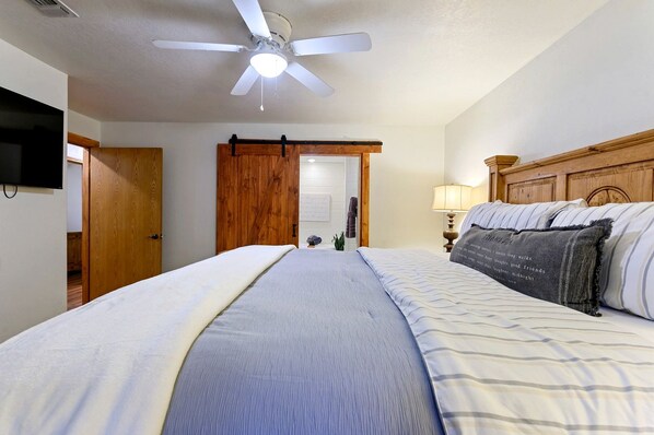 Un dormitorio con cama, ventilador de techo, televisión y puerta de madera.