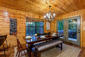 A wooden interior with a dining table set for four, a chandelier, and a view through large windows. - Wonderful Cabin Perfect for Family Getaways in Broken Bow, Oklahoma (Broken Bow)