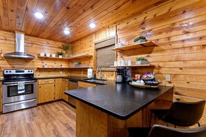 A kitchen with wooden walls, a stove, a sink, and a coffee maker. - Wonderful Cabin Perfect for Family Getaways in Broken Bow, Oklahoma (Broken Bow)