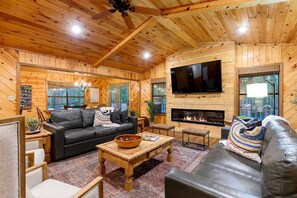 A cozy log cabin interior with a fireplace, leather sofas, a TV, and wooden walls. - Wonderful Cabin Perfect for Family Getaways in Broken Bow, Oklahoma (Broken Bow)