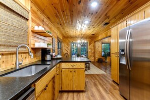 Interior de madera con cocina, que incluye un refrigerador de acero inoxidable, armarios de madera, una encimera negra y un lavamanos.
