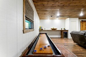 A shuffleboard table in a room with wooden flooring, a window, and a couch. - Wonderful Cabin Perfect for Family Getaways in Broken Bow, Oklahoma (Broken Bow)