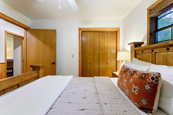 Un dormitorio con cama, un armario de madera, una mesita de noche con lámpara y una ventana con vistas.