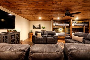 Ein gemütliches Wohnzimmer mit einem Ledersofa, einem Relaxsessel, einem Fernseher und einem Hochbett im Hintergrund.