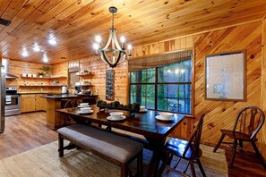 A wooden cabin interior with a dining area, kitchen, and a large window with a view of the outdoors. - Wonderful Cabin Perfect for Family Getaways in Broken Bow, Oklahoma (Broken Bow)
