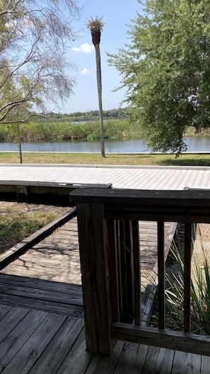 Een houten terras met uitzicht op een rustig waterlichaam, omringd door bomen en onder een heldere lucht.